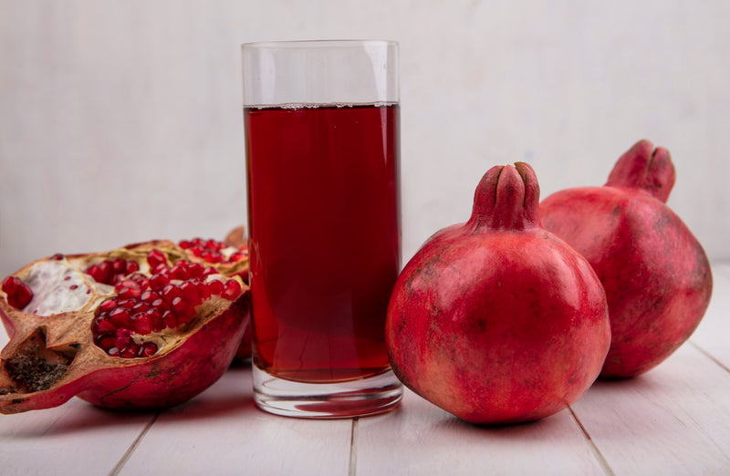 glass of pomegranate juice with pomegranates on white wall